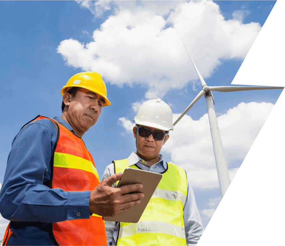 Two men in hard hats and vests standing next to a wind turbine.